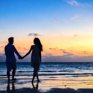 man and woman holding hands walking on seashore during sunrise