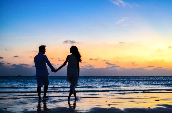 man and woman holding hands walking on seashore during sunrise